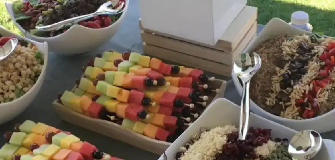Outdoor event buffet with fruit skewers, grain salads and fresh flowers