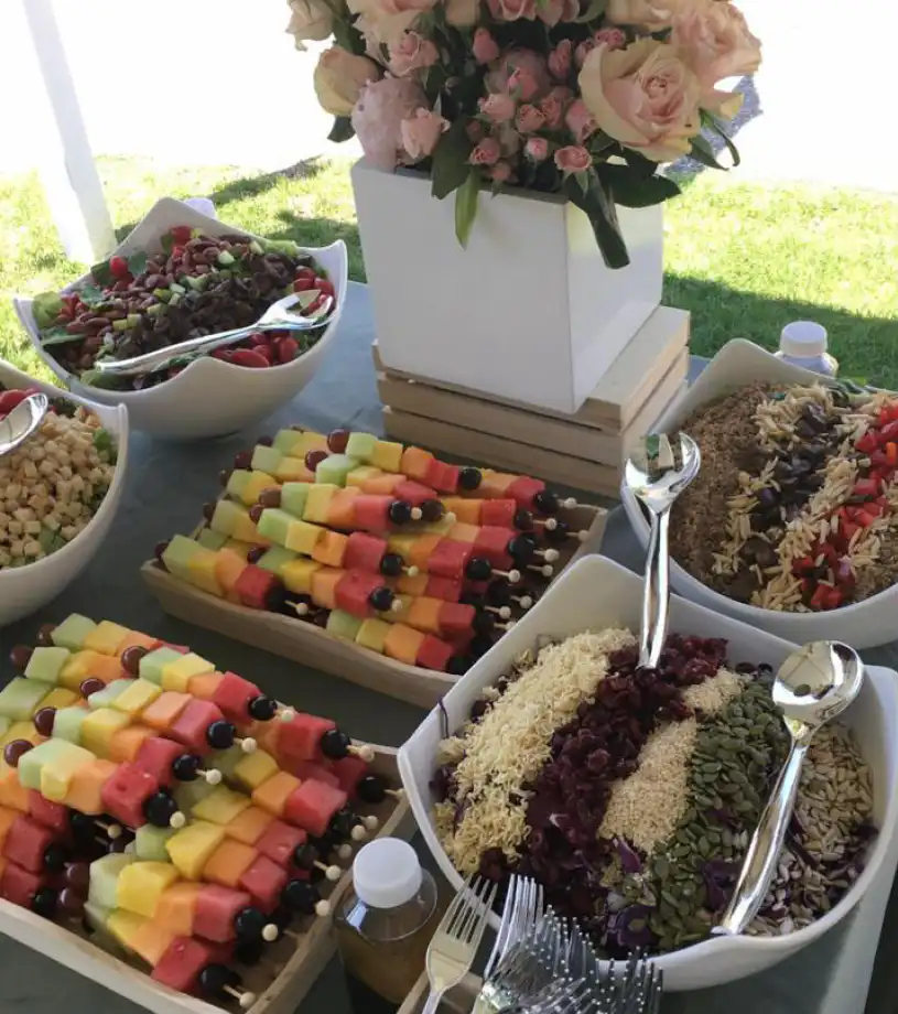 Outdoor event buffet with fruit skewers, grain salads and fresh flowers